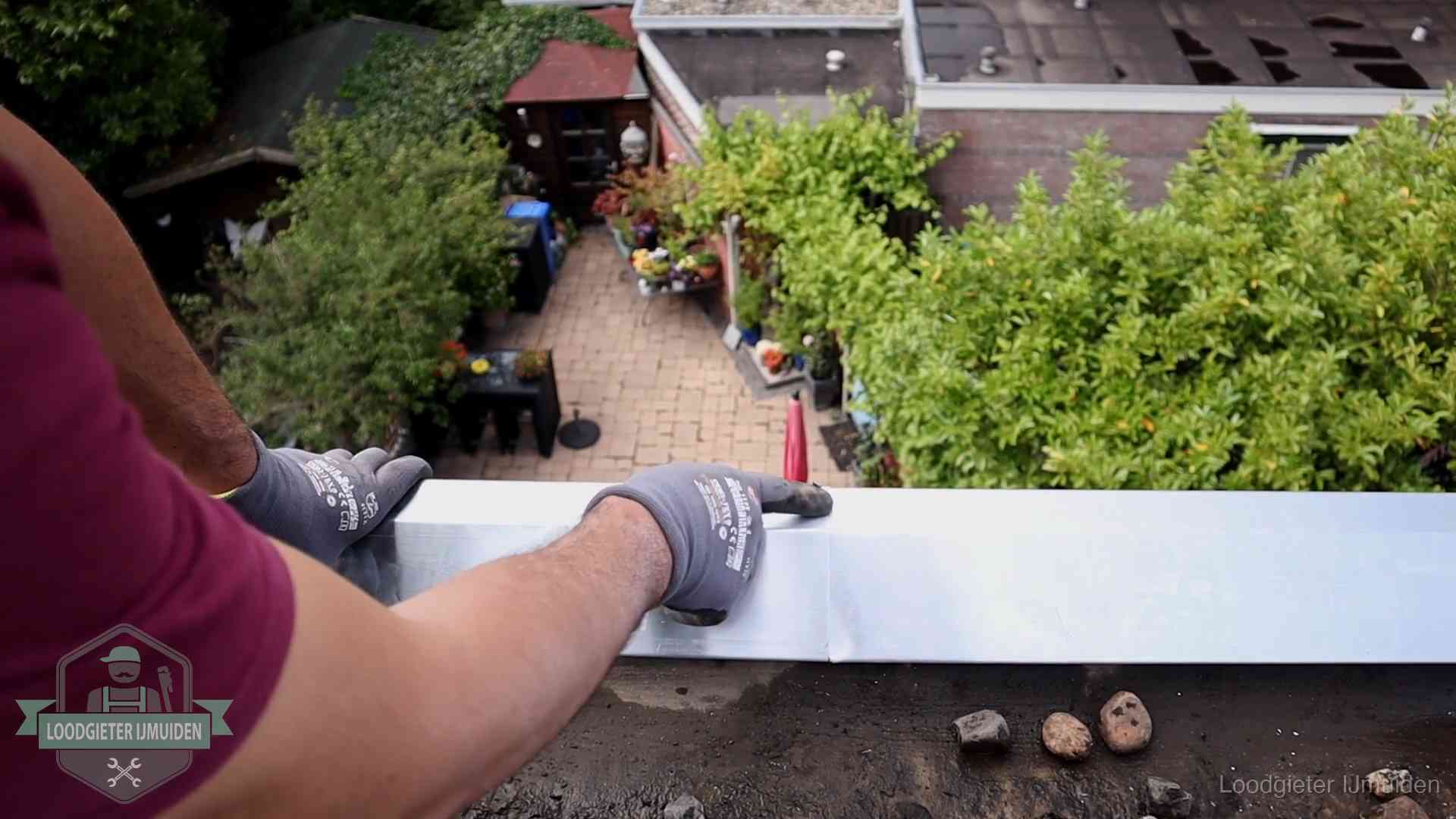 Vakman plaatst een daktrim op de dakrand van een woning in IJmuiden