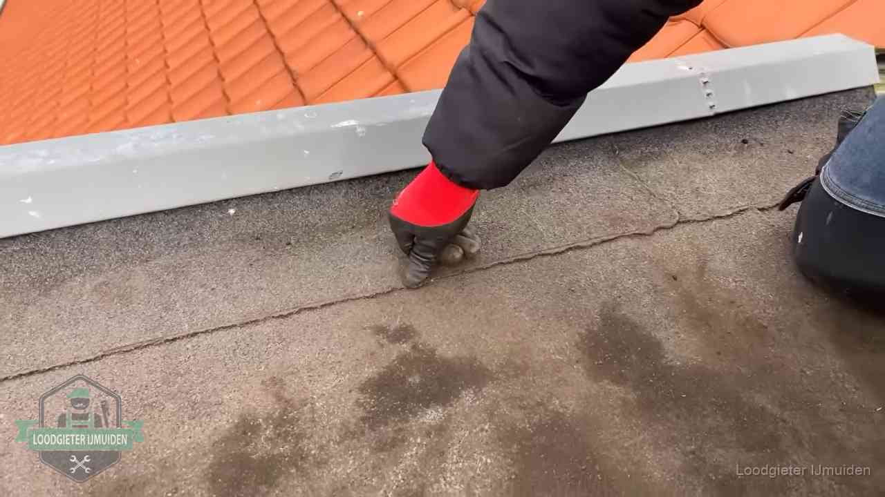 Vakman wijst een naad met vochtplekken aan op een bitumen plat dak in IJmuiden