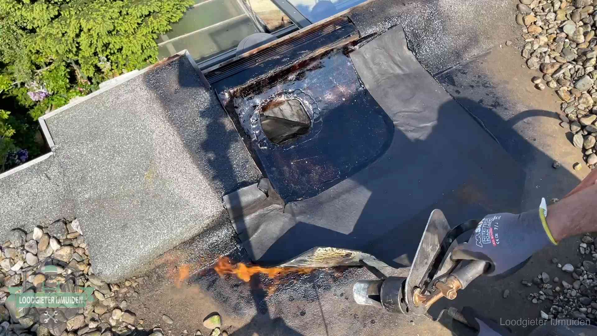 Dakdekker brandt bitumen rond een doorvoer tijdens een daklekkage-reparatie in IJmuiden