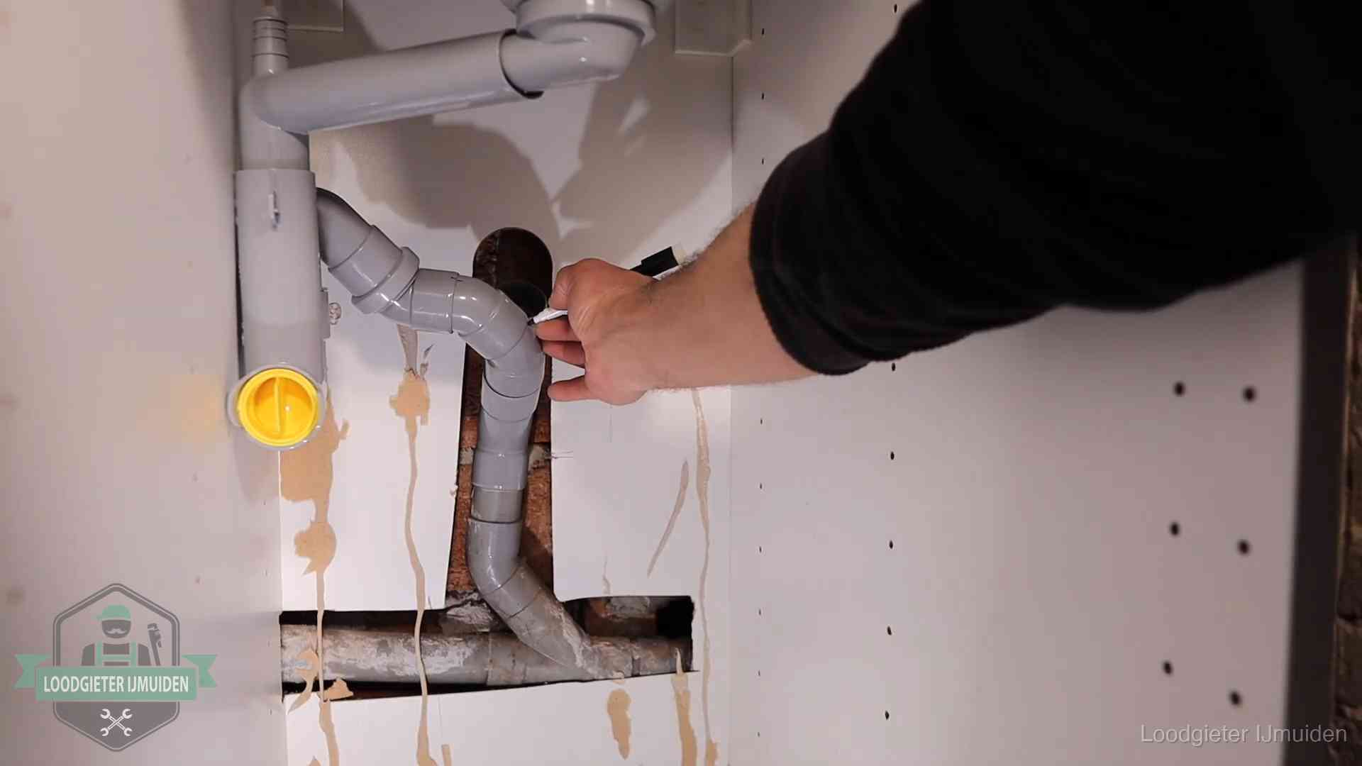 Loodgieter voor verhuurders en bedrijven in IJmuiden Loodgieter markeert een pvc-afvoerbuis onder een gootsteen in IJmuiden