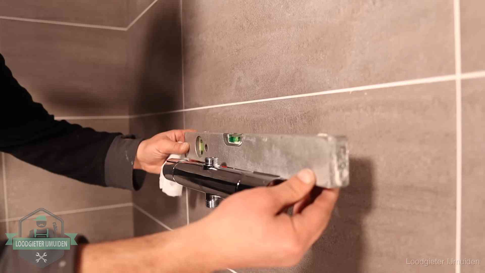 Loodgietersbedrijf voor sanitair in IJmuiden Loodgieter lijnt een douchekraan uit met een waterpas in een woning in IJmuiden