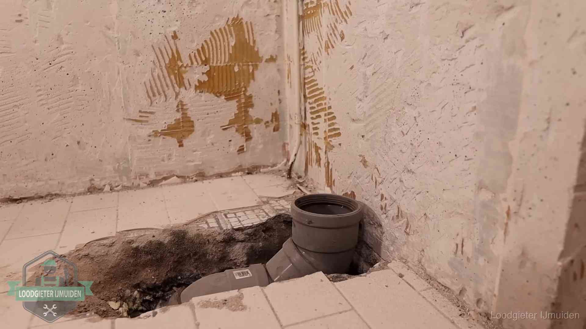 Verzakt riool herstellen in IJmuiden Opengebroken vloer met een nieuwe pvc-rioolbocht in een gegraven sleuf in IJmuiden