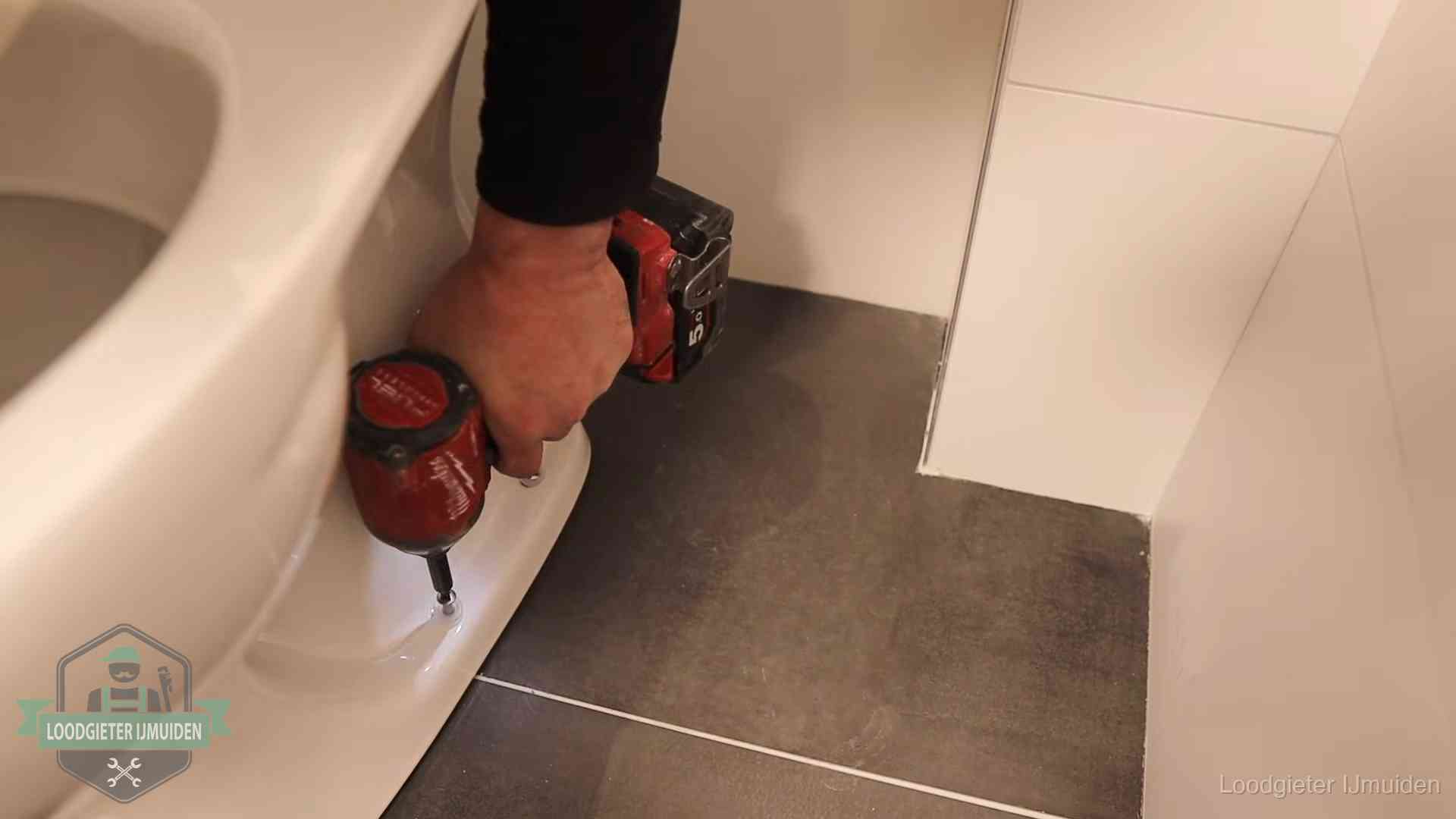 Loodgieter zet de voet van een wc-pot vast op de tegelvloer in IJmuiden